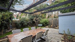 A wooden table with six chairs, a wooden pergola, a garden with a wooden fence, and a shed. - Host Stay Cragg Cottage (Whitby)