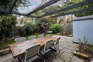 Relax in a shaded patio area surrounded by lush greenery and a wooden pergola.