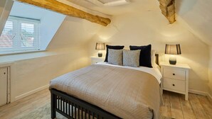 A bedroom with a sloped ceiling, a skylight, a bed with a headboard, two bedside tables with lamps, and a window with blinds. - Host Stay Cragg Cottage (Whitby)