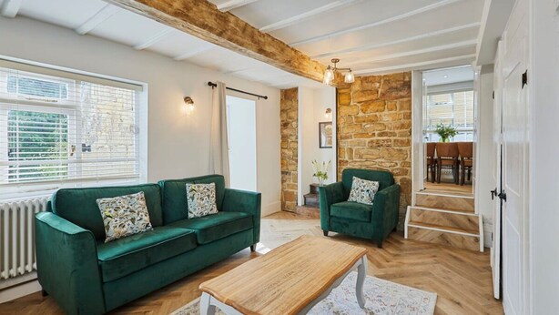 A spacious living room with a green sofa, a wooden coffee table, and a stone wall. - Host Stay Cragg Cottage (Whitby)