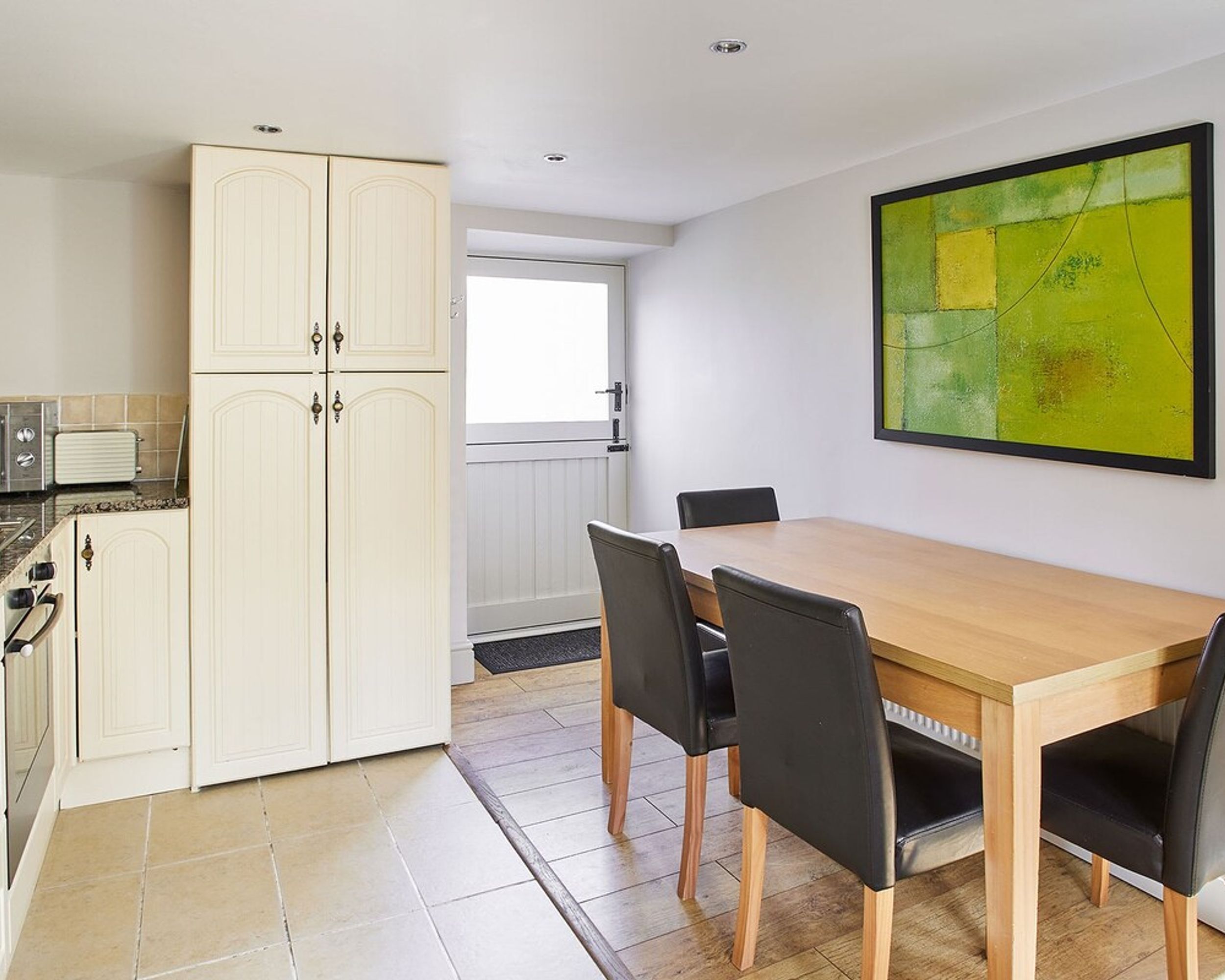 A modern kitchen with white cabinetry, a wooden dining table with four chairs, and a large abstract painting on the wall.
