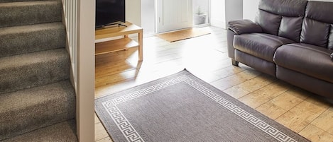 A living room with a staircase, a television, a leather sofa, and a patterned rug.