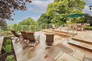 An outdoor patio with stone flooring, wooden lounge chairs, and a green umbrella. - Host Stay The View at Orchard View (Ashbourne)