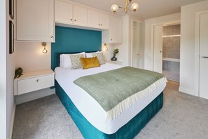 Une chambre à coucher avec un lit, des armoires blanches, une tête de lit de couleur turquoise et une petite table de chevet avec une lampe.