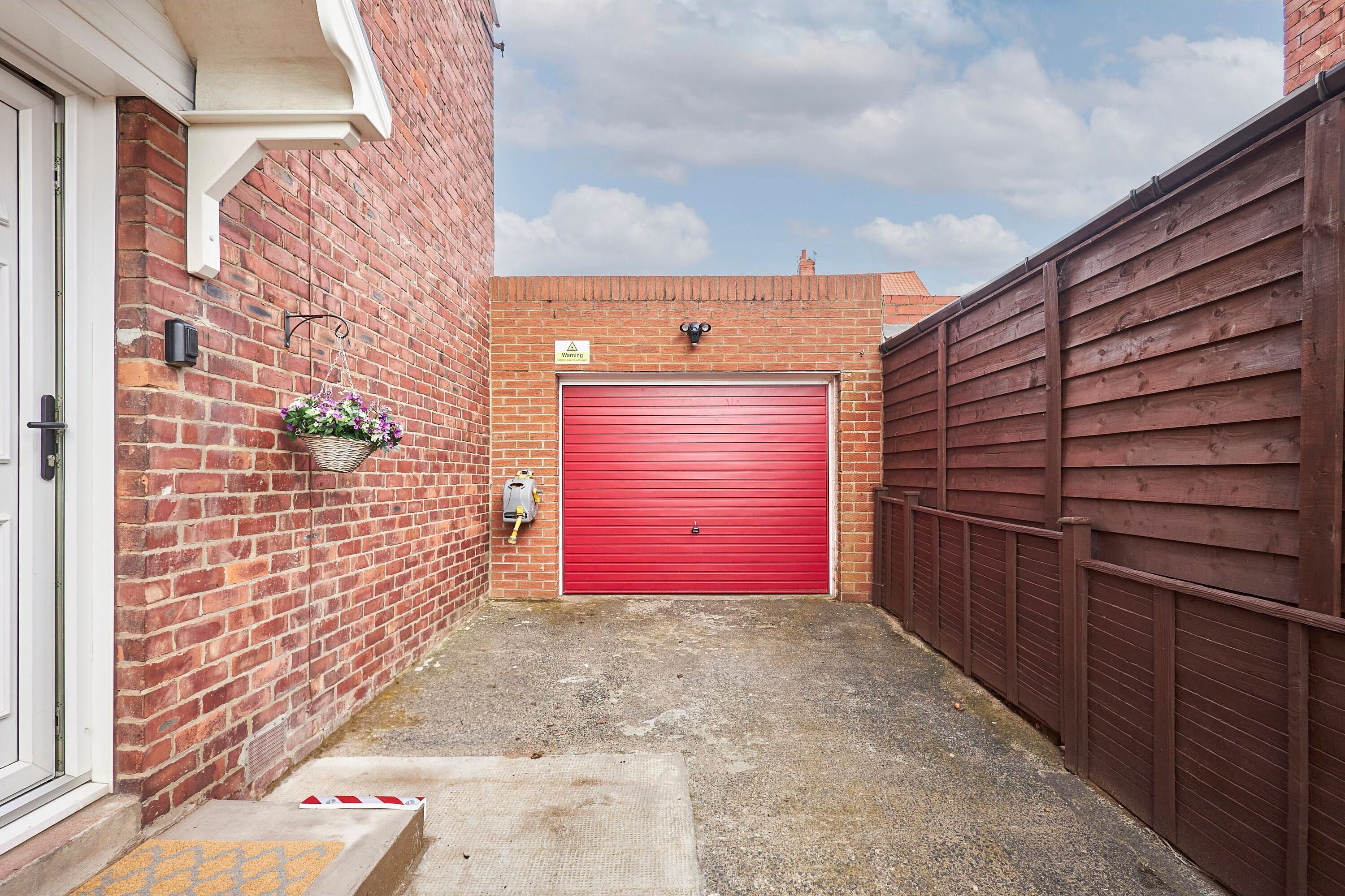 A narrow alleyway with a red garage door, a brick wall, and a wooden fence.
