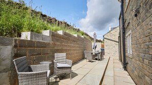 An outdoor patio with wicker furniture and a stone wall. - Host Stay Clackgill Cottage (Harrogate)