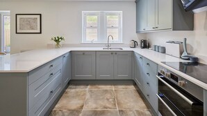 A modern kitchen with grey cabinets, a large island, a built-in oven, and a window above the sink. - Host Stay Clackgill Cottage (Harrogate)