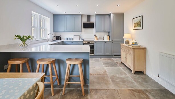 A modern kitchen with a central island, wooden stools, and a dining table. - Host Stay Clackgill Cottage (Harrogate)