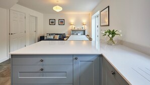 A modern kitchen with a central island, white cabinetry, and a dining area with a table and chairs. - Host Stay Clackgill Cottage (Harrogate)