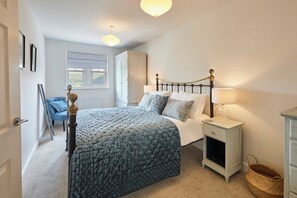 Un dormitorio con cama, mesita de noche, lámpara, silla y ventana con vistas.