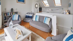 A modern living room with a grey sofa set, a white coffee table, and a bookshelf. There are two skylights and a view of the sky. - Host Stay The Hideaway (Scarborough)