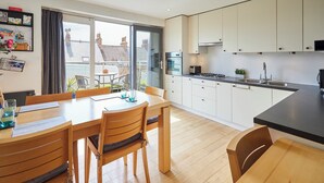 A modern kitchen with white cabinets, a black countertop, and a dining area with wooden furniture. - Host Stay The Hideaway (Scarborough)