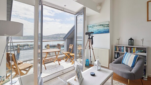 A spacious balcony with a view of the sea, a telescope, and a cozy seating area with a bookshelf and a lamp. - Host Stay The Hideaway (Scarborough)