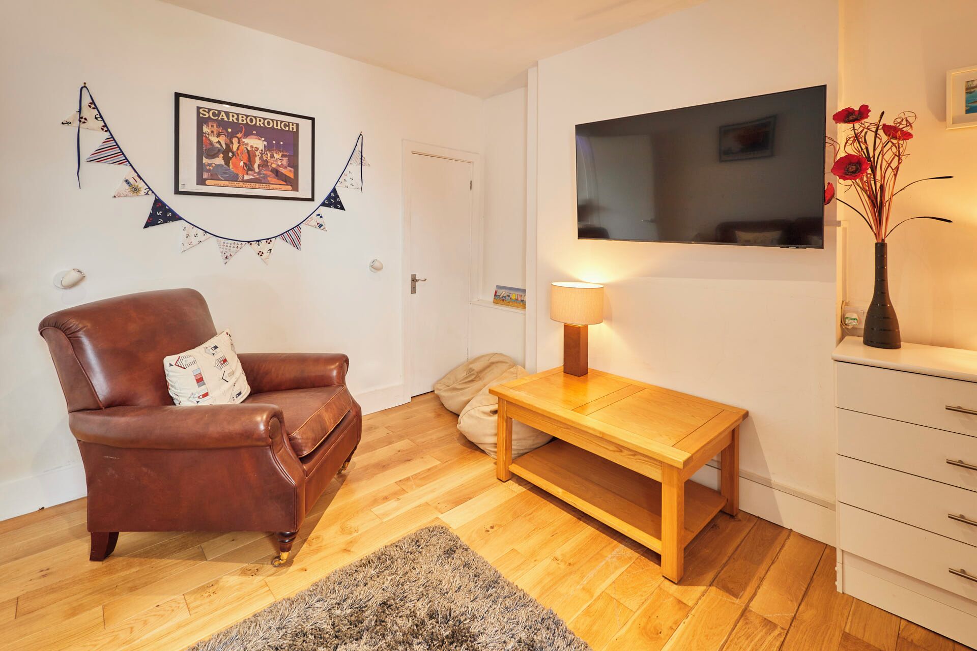 Une pièce chaleureuse avec un fauteuil en cuir marron, une table en bois avec une lampe, un téléviseur fixé au mur et une décoration murale.