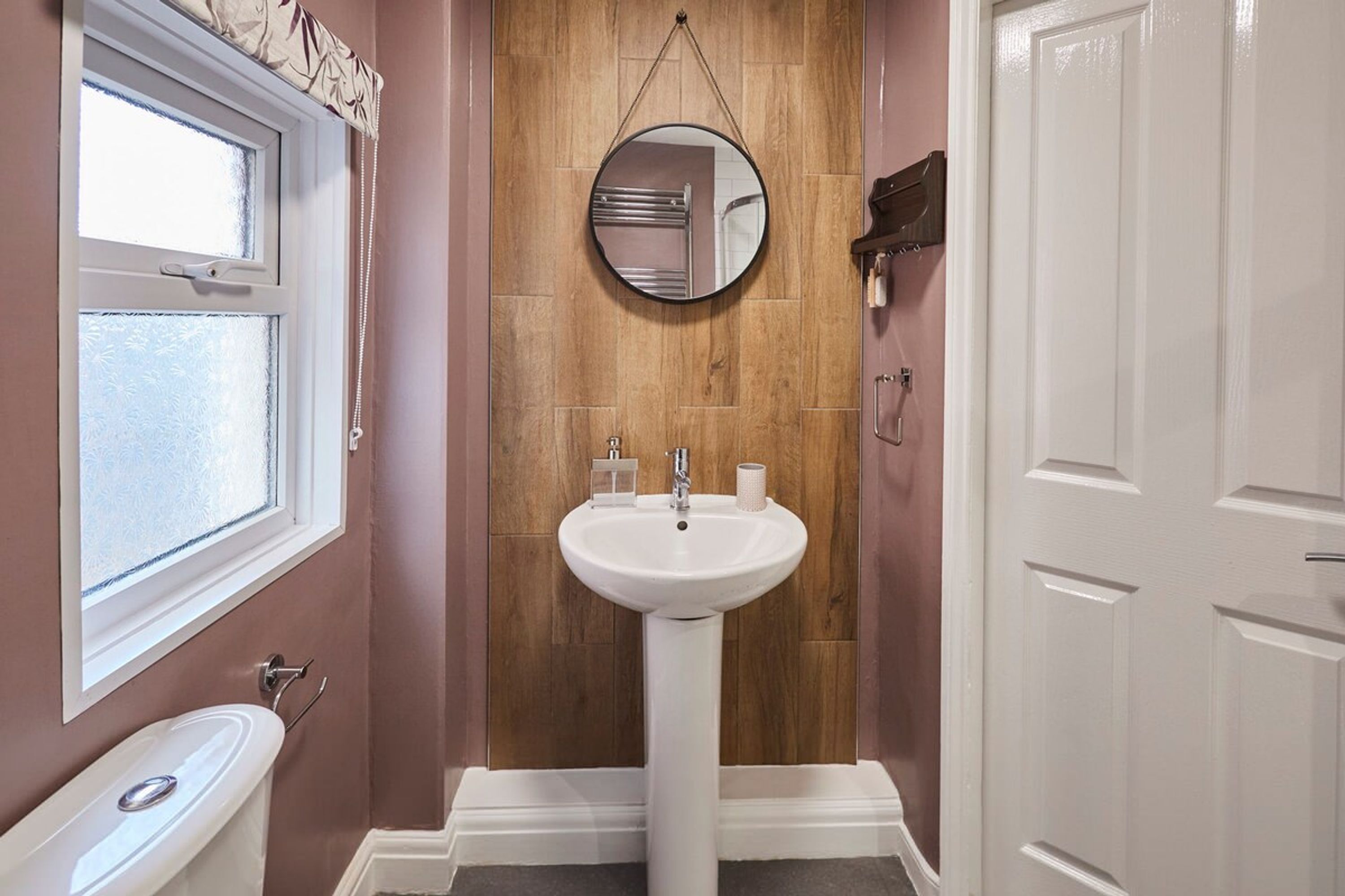 Une salle de bain avec un lavabo sur colonne blanc, une fenêtre et un mur en bois.