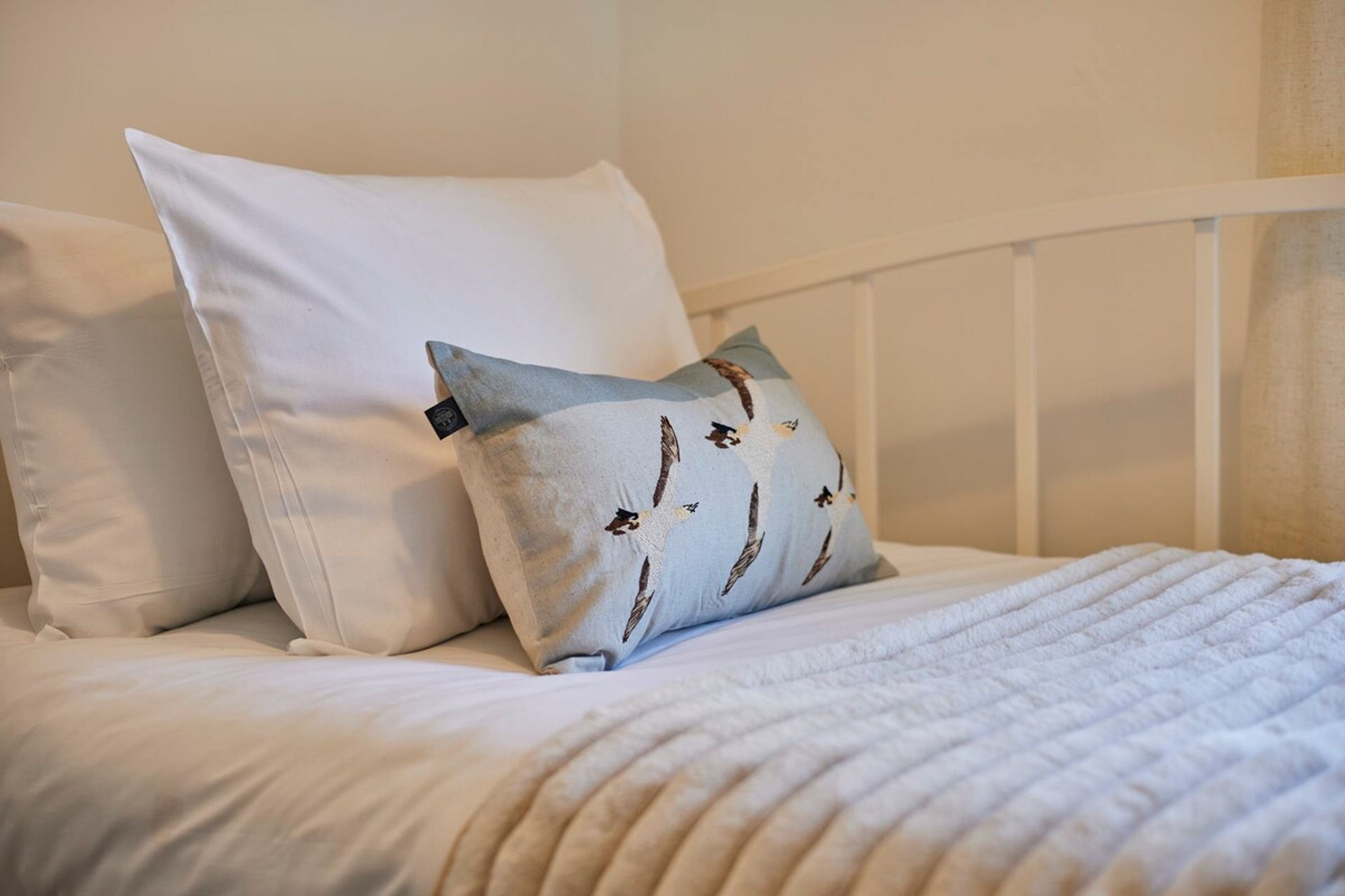 A bed with white bedding and a pillow with a bird pattern.