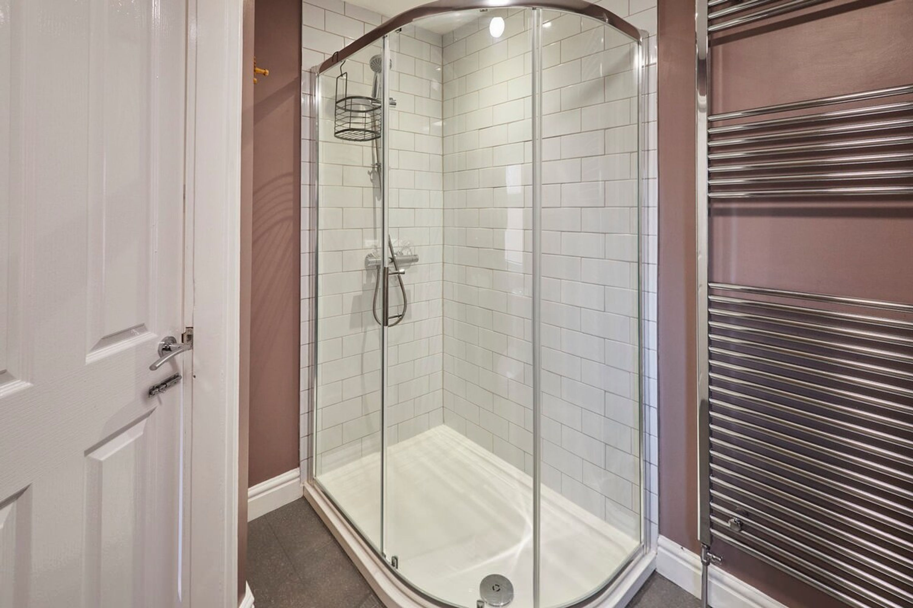 Ducha con cerramiento de vidrio, pared de azulejos blancos, un cabezal de ducha y un accesorio de ducha de mano.