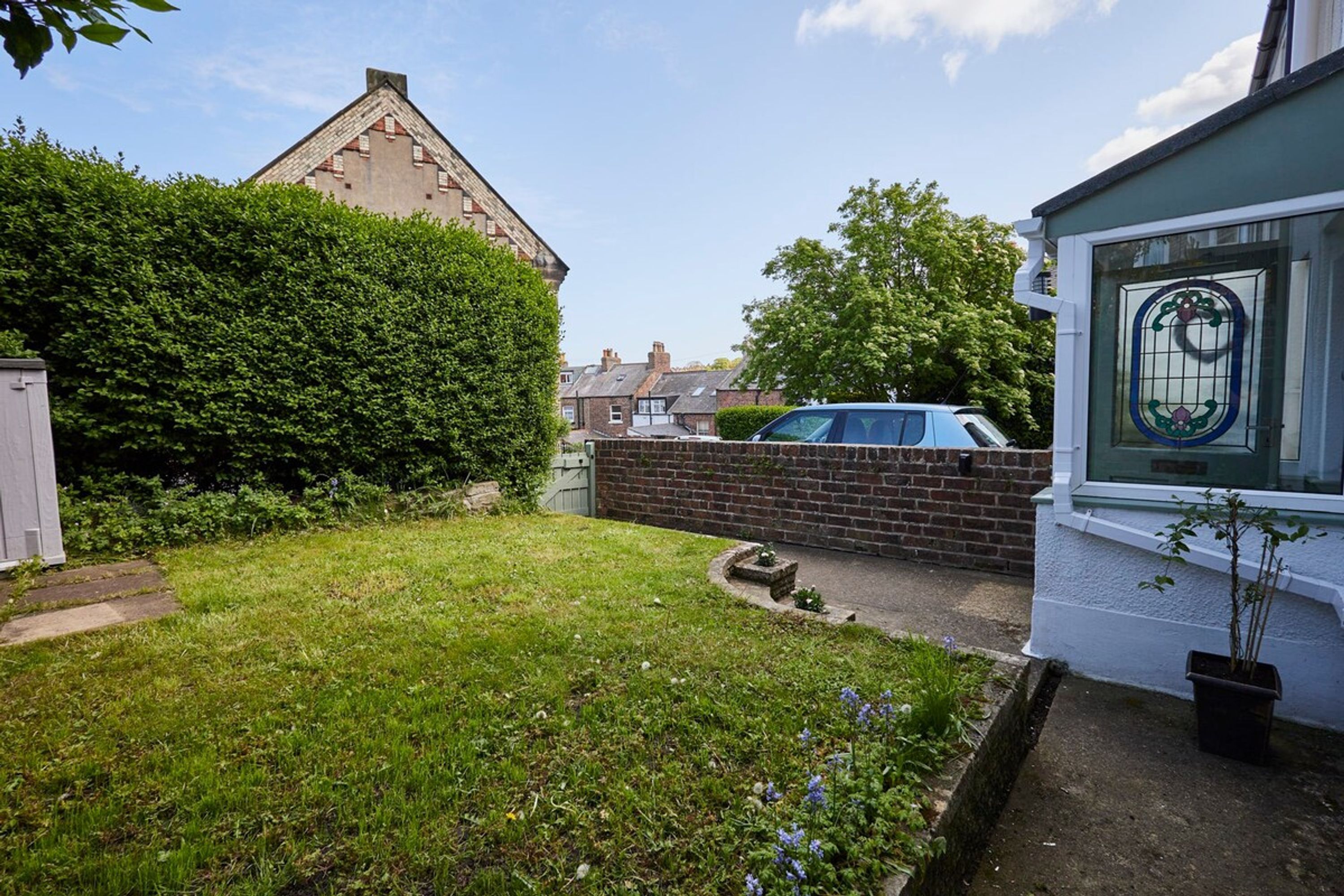 A residential garden with a brick wall, a hedge, and a car parked in the background.