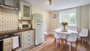 La cuisine est équipée d’un four à micro-ondes, d’un four traditionnel et d’un réfrigérateur. On y trouve une table à manger avec des chaises, ainsi qu’une horloge au mur.