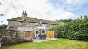 Une maison en pierre avec un toit en tuiles, une clôture en bois et une terrasse aménagée avec du mobilier d’extérieur.