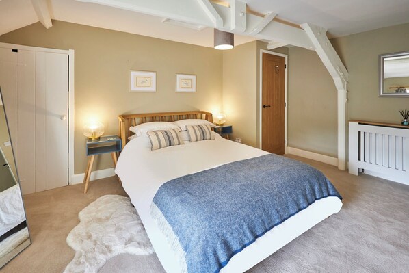 A bedroom with a large bed, two bedside tables with lamps, a wooden door, and a radiator. - Host Stay North Cottage (Hexham)