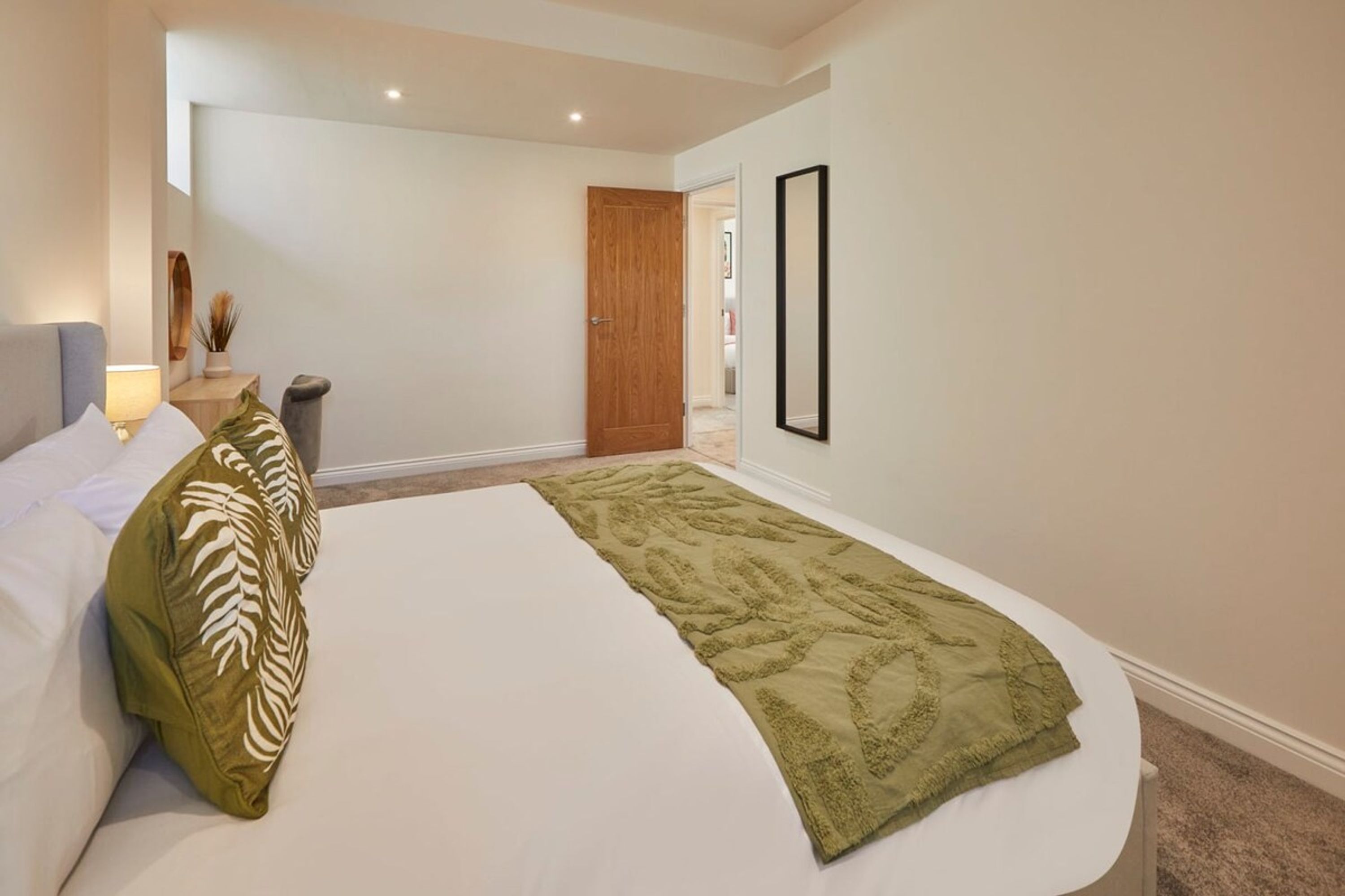 Un dormitorio con una cama, una mesita de noche, una lámpara, una puerta y un espejo en la pared.