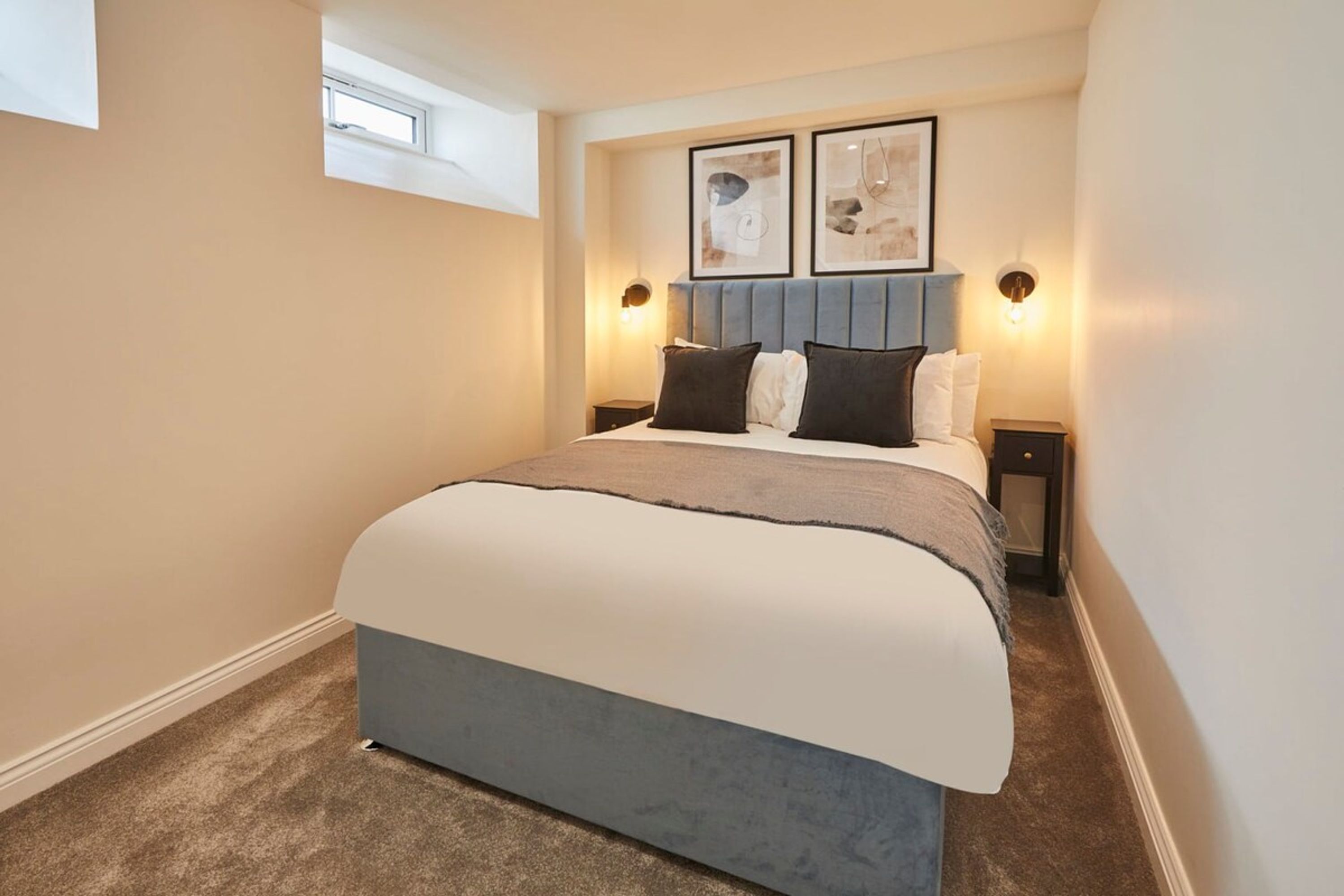 A bedroom with a bed, headboard, bedside tables, wall art, and a window.
