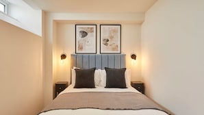 Un lit bien fait, avec une tête de lit bleue, deux appliques murales et deux œuvres d’art abstraites encadrées au-dessus du lit.