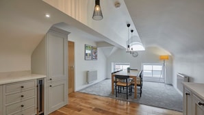 Une pièce mansardée spacieuse, dotée d’une table et de chaises, d’un plancher en bois et d’un plafond en pente agrémenté de luminaires suspendus.
