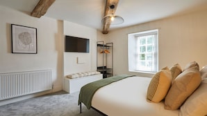 A bedroom with a bed, a radiator, a TV, a window with blinds, and a wooden beam ceiling. - Host Stay Stay House (Thirsk)