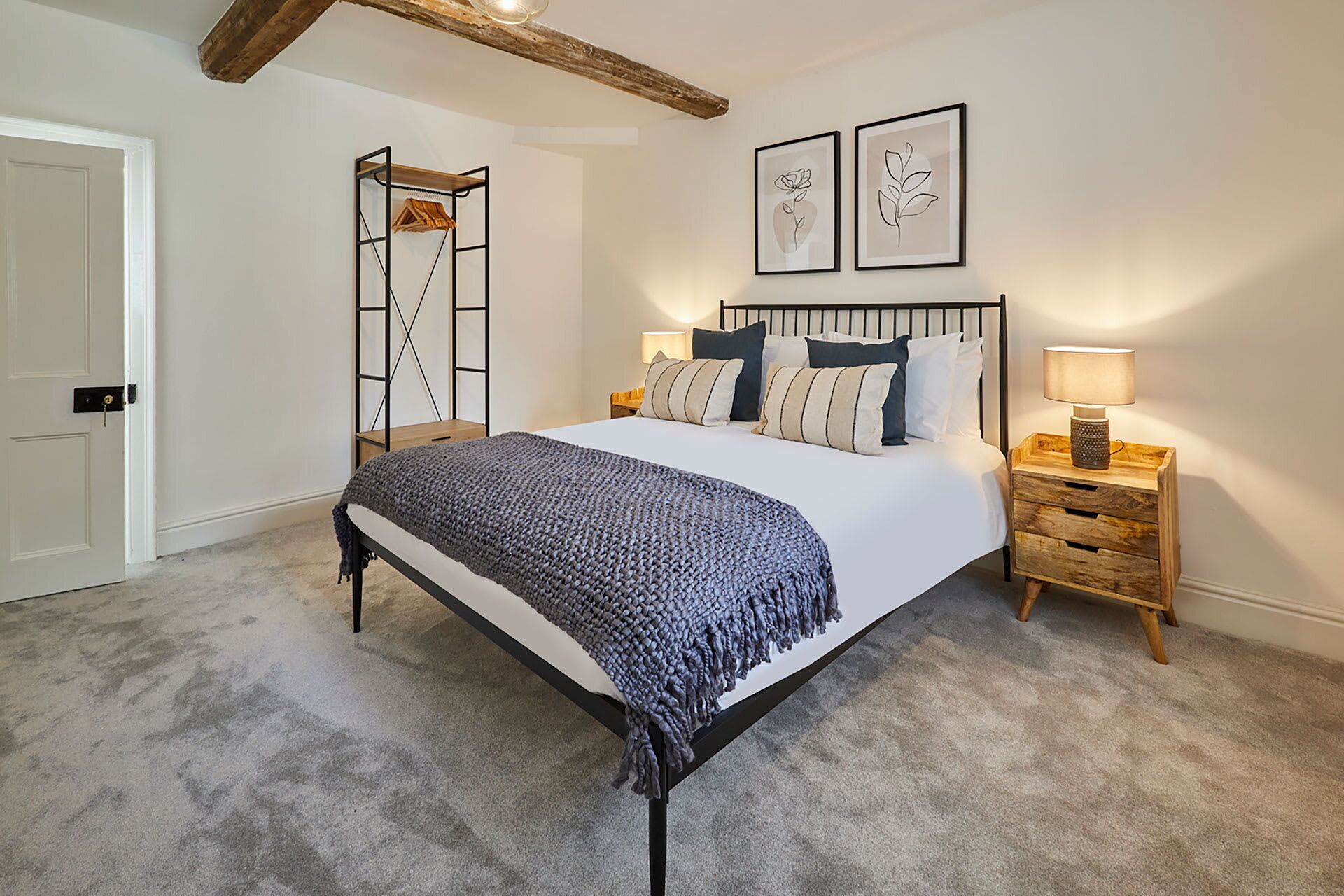 A bedroom with a bed, a wooden nightstand, a wall-mounted shelf, and two framed pictures.