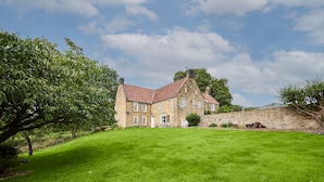 A large stone building with a red-tiled roof, surrounded by a well-maintained lawn and a stone wall. - Host Stay Stay House (Thirsk)