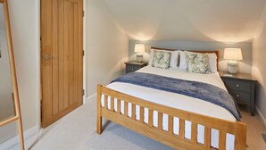 A bedroom with a wooden bed, two bedside tables, a nightstand, a wooden door, and a sloped ceiling. - Host Stay Breckon Cottage (Whitby)