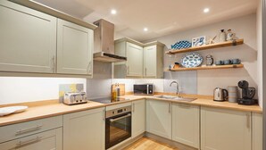 A modern kitchen with light-colored cabinets, a wooden countertop, a built-in oven, a microwave, and a coffee maker. - Host Stay Breckon Cottage (Whitby)