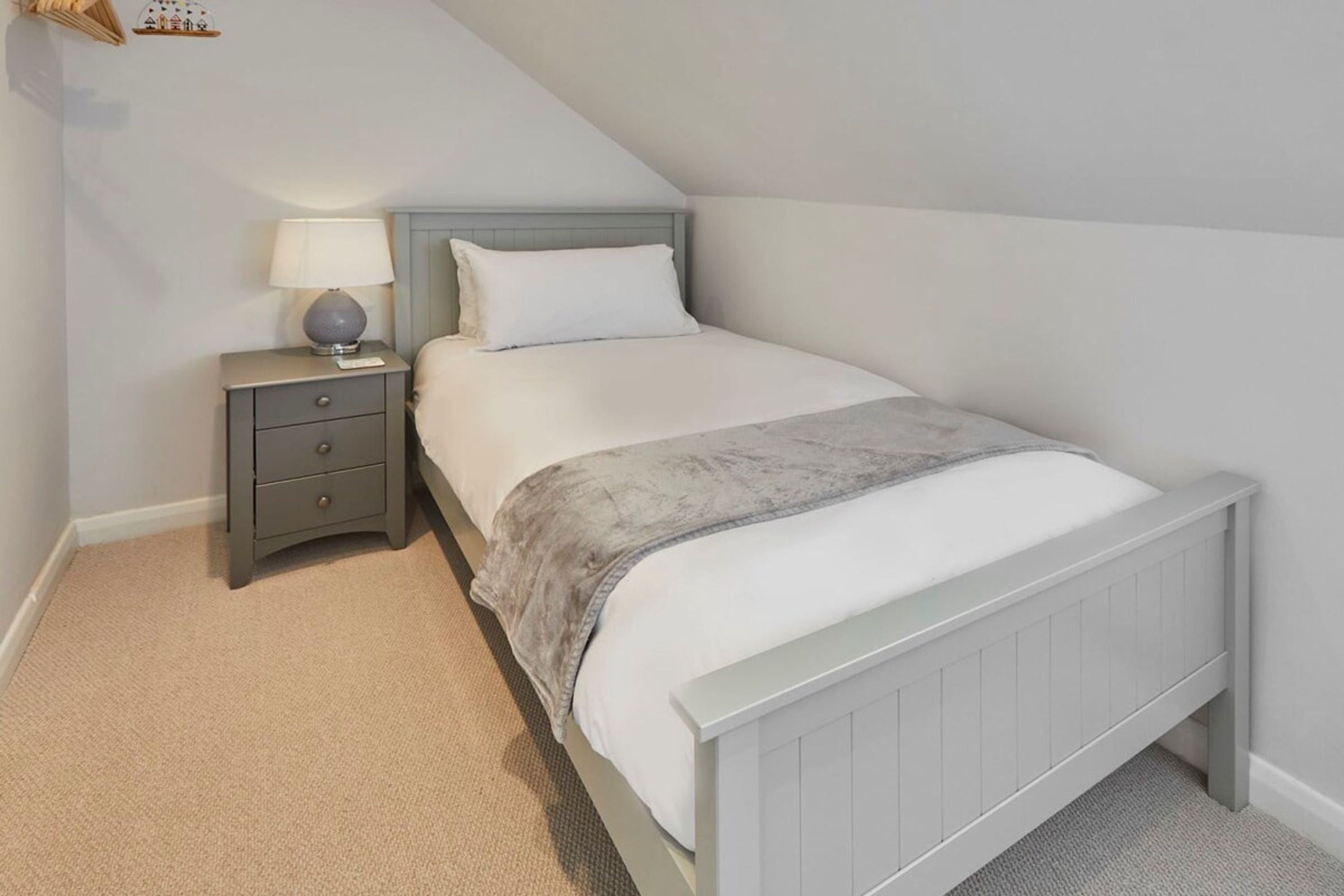 Een slaapkamer met een bed, nachtkastje, lamp en een klein decoratief object aan de muur.