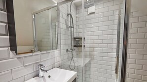 A modern bathroom with a white-tiled shower enclosure, a glass door, and a white sink with a chrome faucet. - Host Stay Breckon Cottage (Whitby)