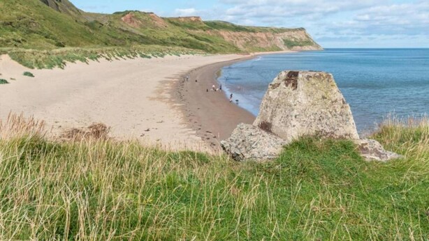 A coastal beach with a large rock formation in the foreground and a sandy beach extending to the water. - Apartments in Skinningrove, Cattersty Sands Beach (Saltburn-by-the-Sea)