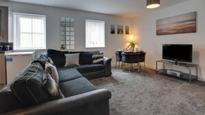 A modern living room with a sectional sofa, a dining table with chairs, a flat-screen TV, and a painting on the wall. - Apartments in Skinningrove, Cattersty Sands Beach (Saltburn-by-the-Sea)