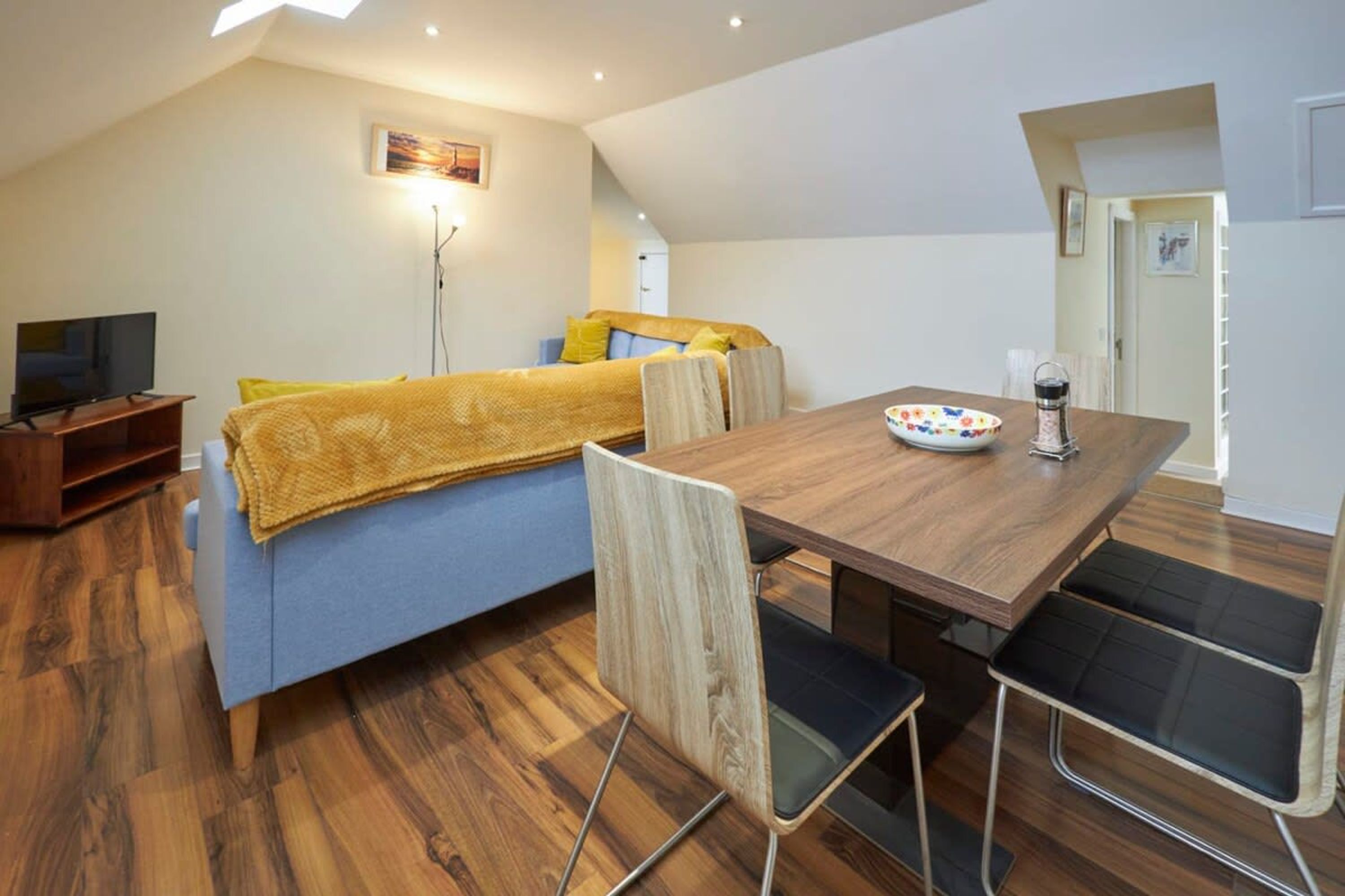 Een moderne woonkamer met een bank, een eettafel met stoelen, een televisie en een vloerlamp.