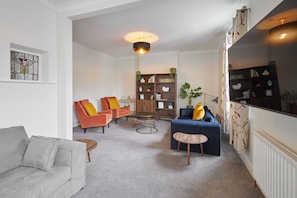 A living room with a grey sofa, two armchairs, a blue sofa, a small round table, and a bookshelf.