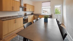 Une cuisine moderne avec des meubles en bois, une hotte en acier inoxydable et un coin repas comprenant une longue table et des chaises.