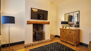 A room with a fireplace, a television mounted above it, a wooden cabinet with a mirror, and a floor lamp. - Host Stay Darcey House (Scarborough)