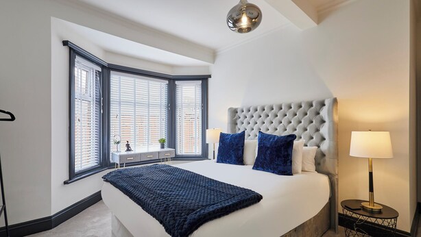 A bedroom with a large bed, a window with blinds, a bedside table with a lamp, and a ceiling light. - Host Stay Darcey House (Scarborough)
