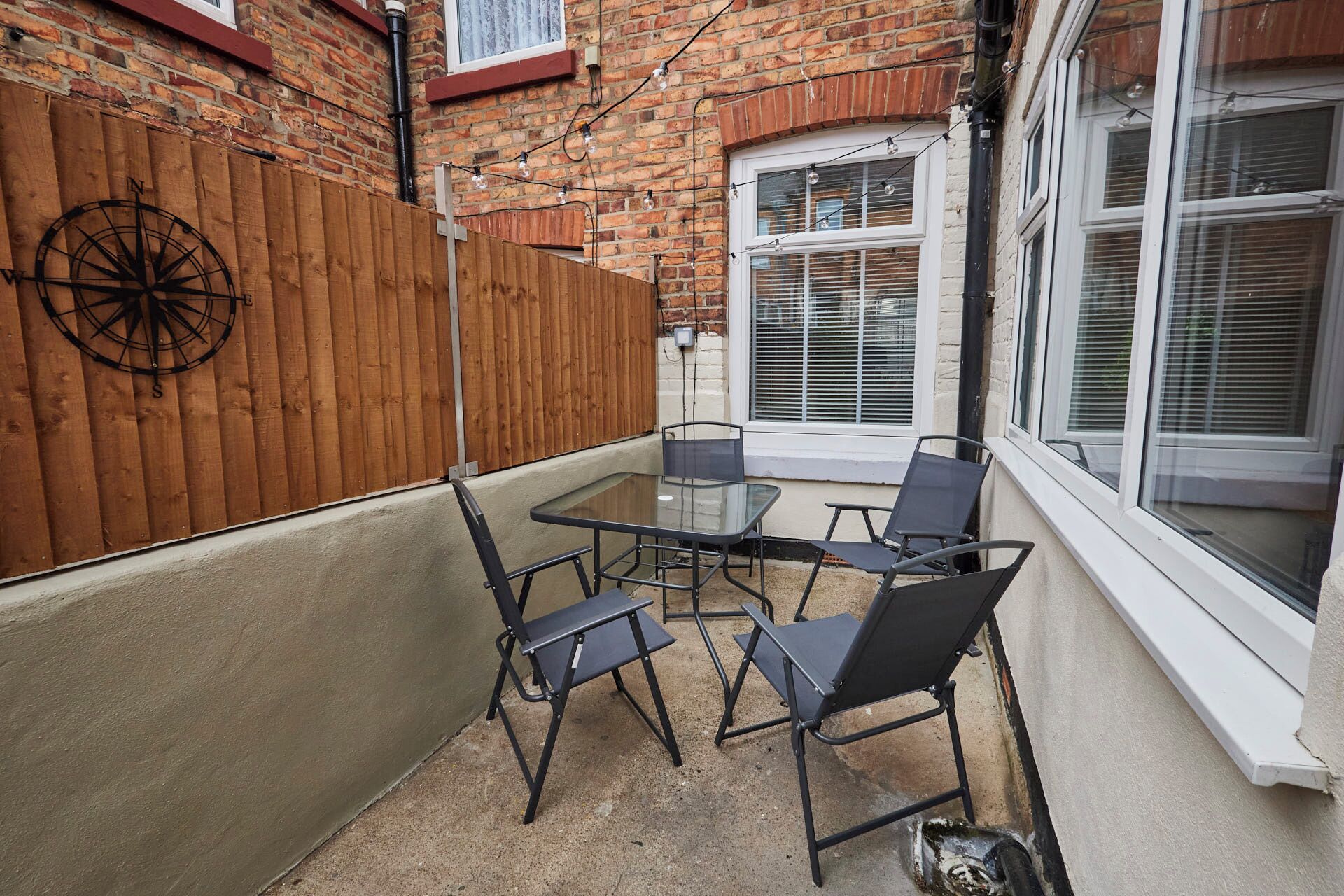 A small patio with a table and chairs, a wooden fence, and a brick wall.