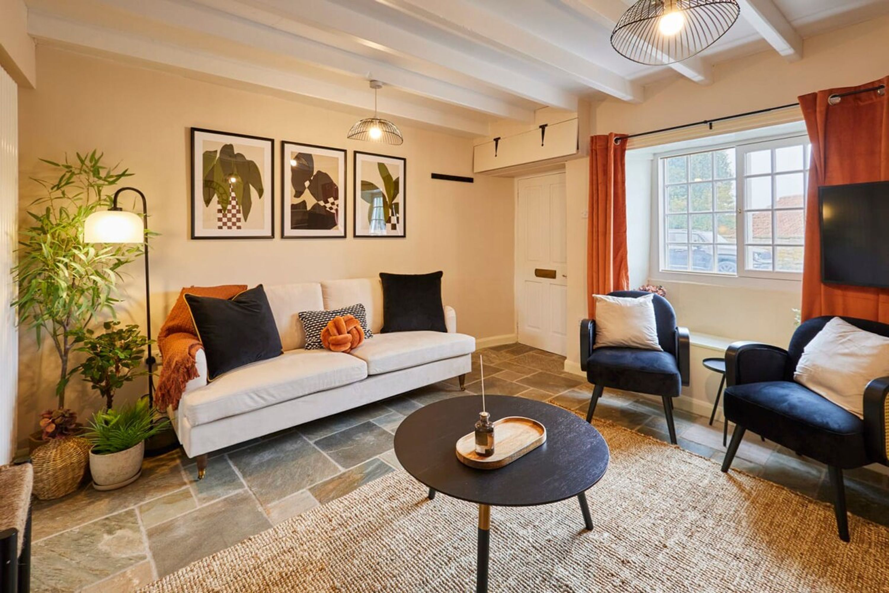 Un salon comprenant un canapé, deux fauteuils, une table basse et un téléviseur. Les murs sont ornés de tableaux encadrés, et on y trouve également une lampe sur pied et une plante en pot.