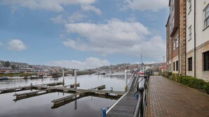 Une vue sur le front de mer, avec un quai, une rivière paisible et un bâtiment doté d’un chemin d’accès en briques.