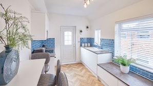A modern kitchen with a herringbone wood floor, white cabinetry, and blue-tiled backsplash. - Host Stay Marshlands (Redcar)