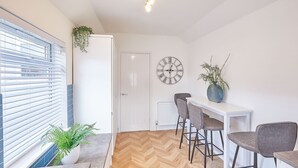 A modern kitchen with a herringbone wood floor, white cabinetry, and a large wall clock. - Host Stay Marshlands (Redcar)