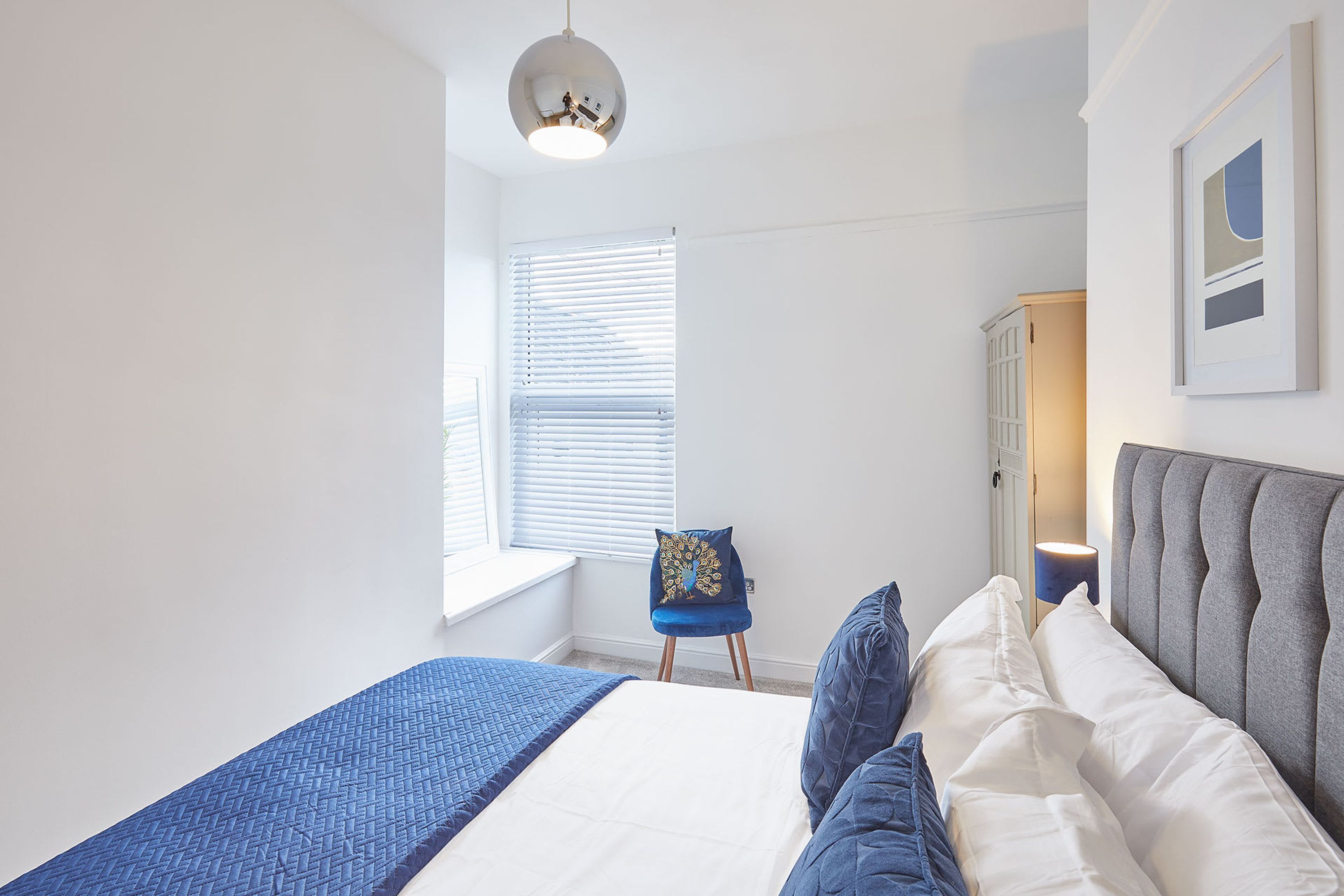 A bedroom with a bed, a chair, a lamp, and a window with blinds.