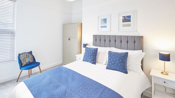 A neatly arranged bedroom with a large bed, a chair, a wardrobe, and a bedside table with a lamp. - Host Stay Marshlands (Redcar)